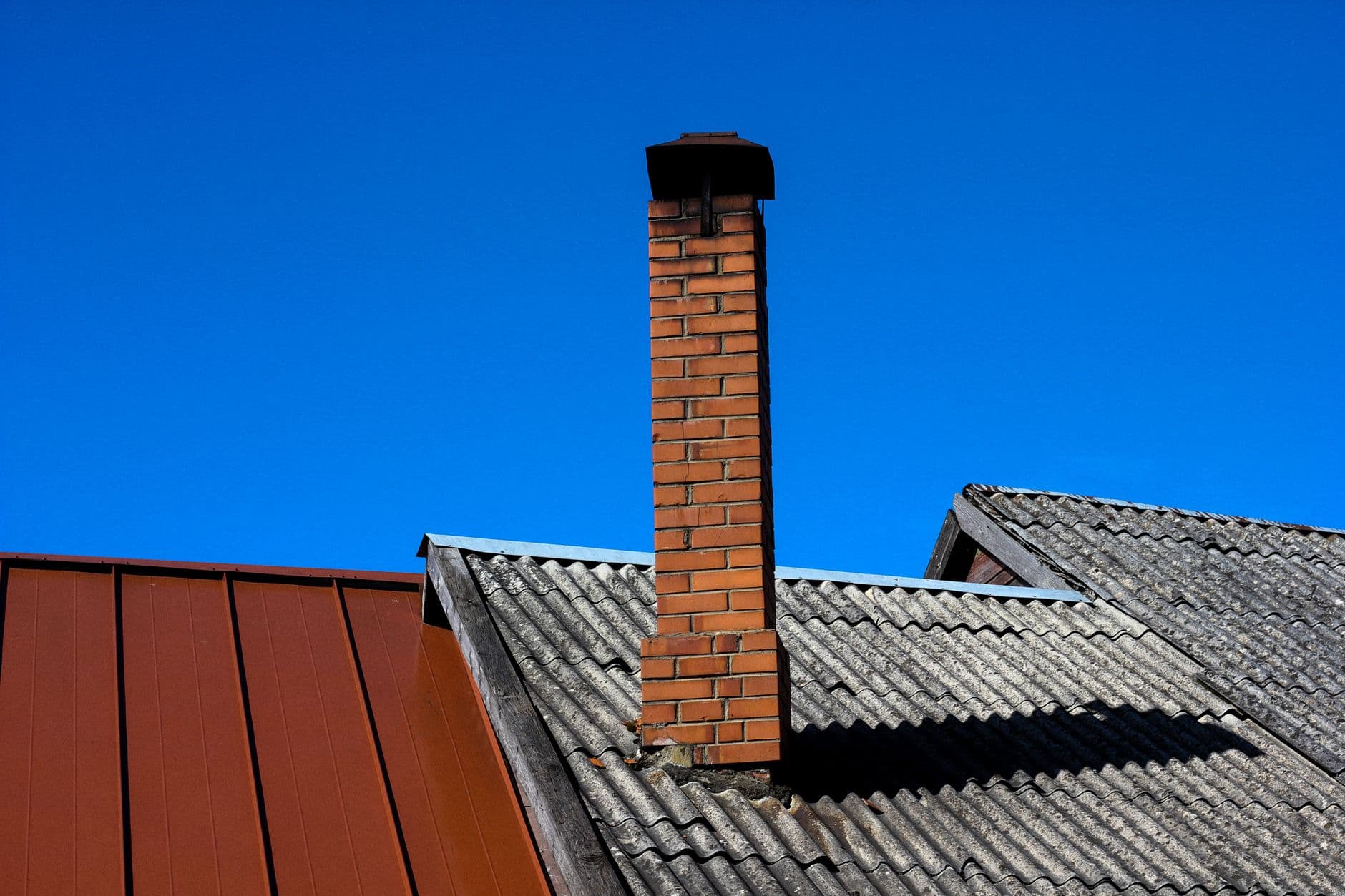 A solitary brick chimney rises from a tiled roof under a vibrant blue sky, showcasing minimal architecture.