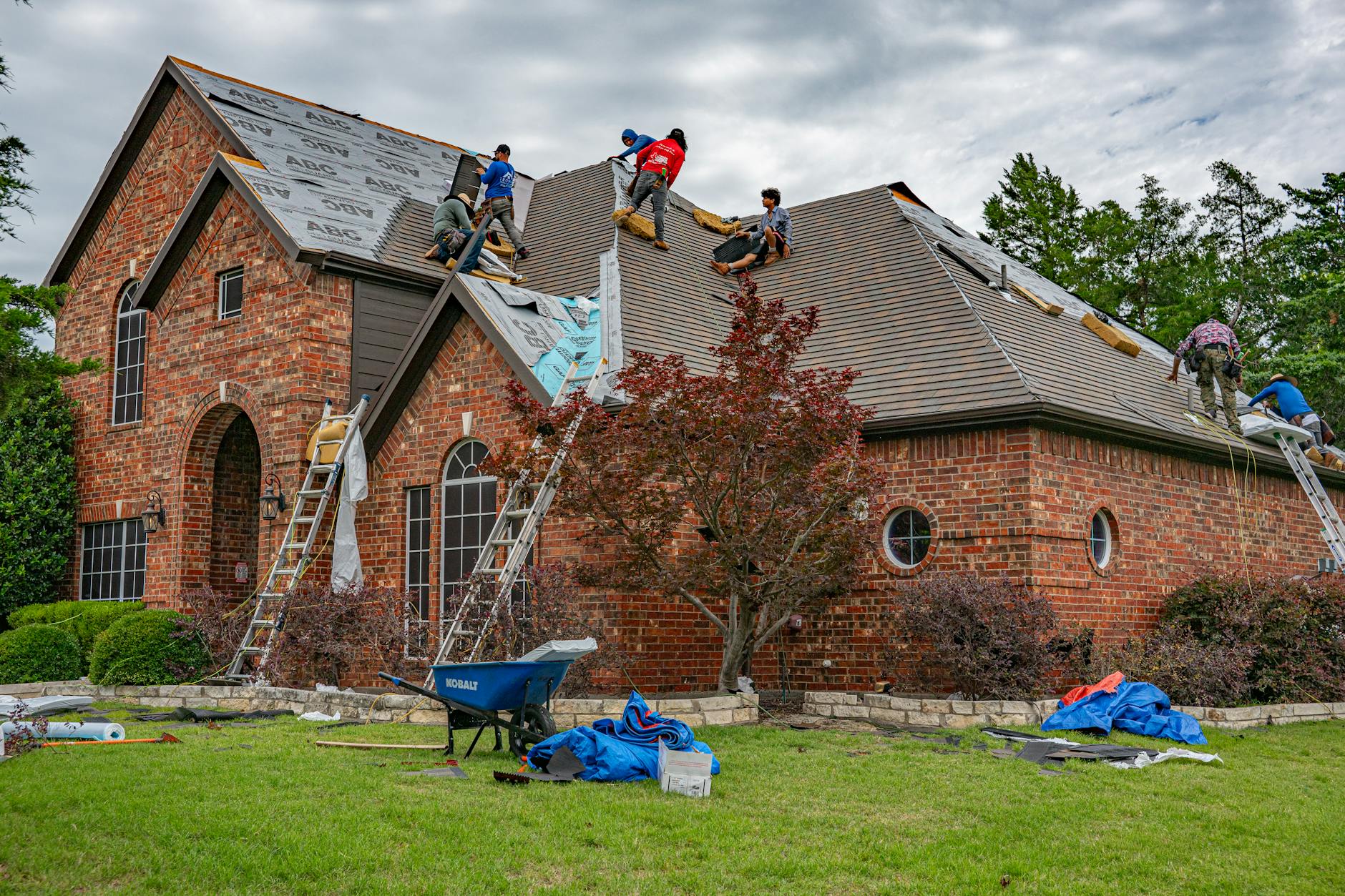 Roofers working on brick home in Allen, Texas, addressing shingles and roofing materials.
